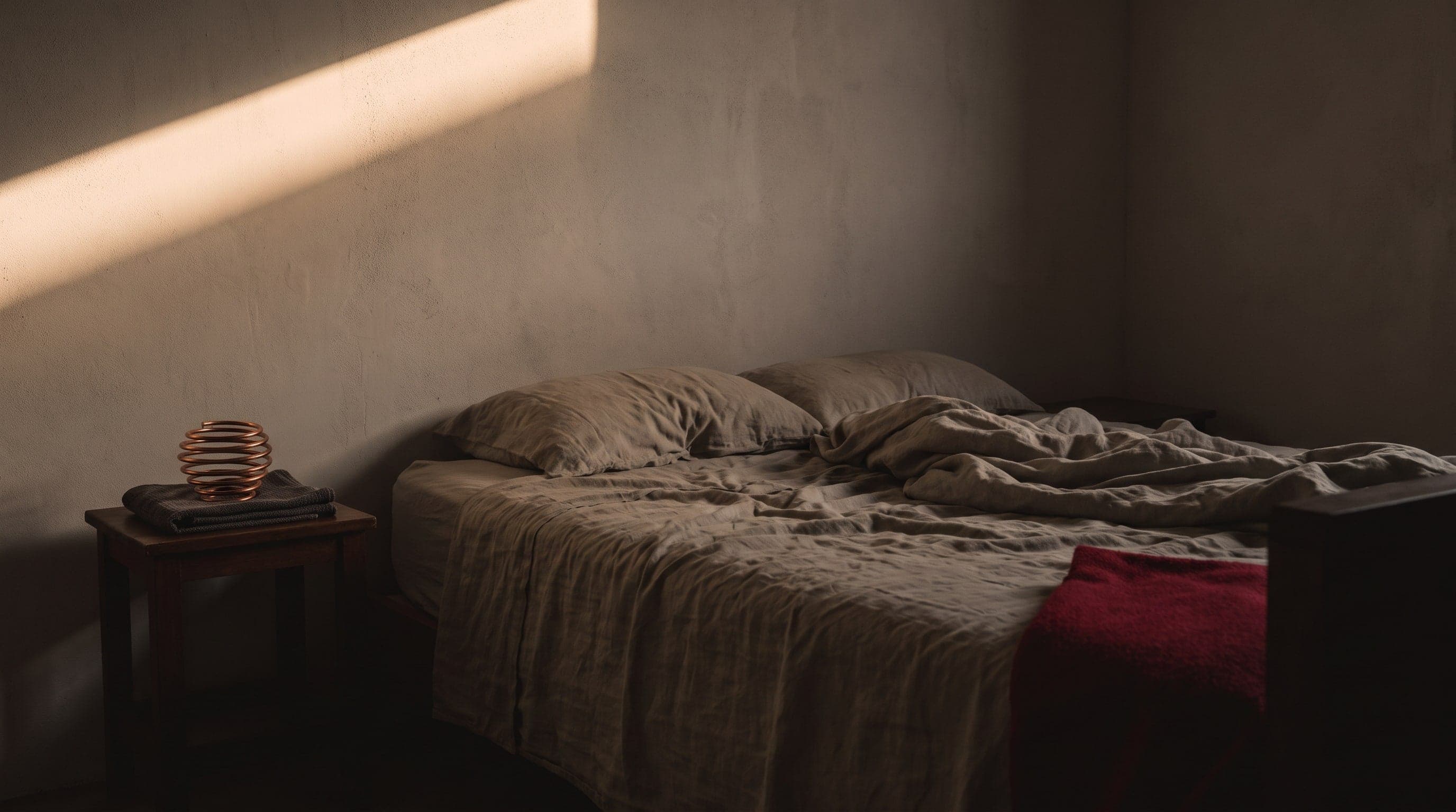 Schlichtes Schlafzimmer im ersten Licht, auf dem Nachttisch liegt eine gewickelte Kupferspirale